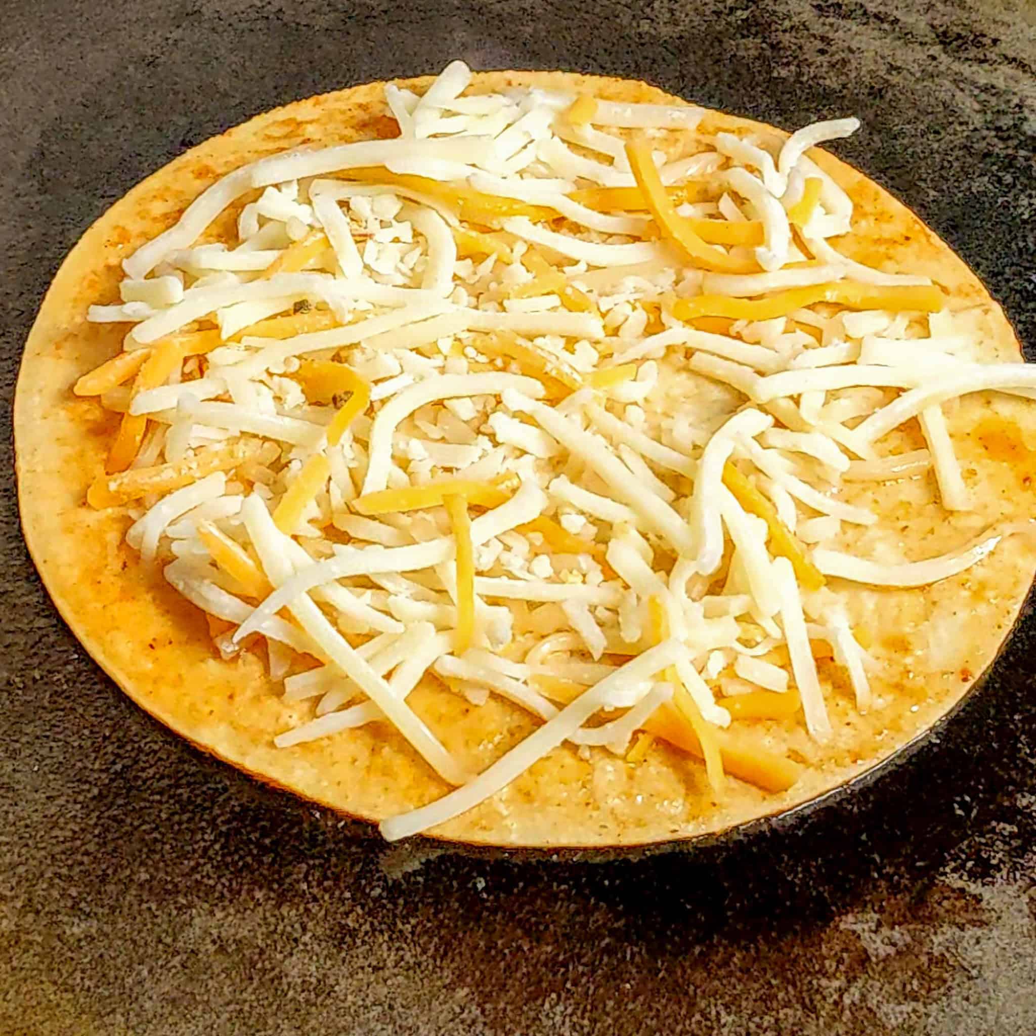 shredded cheese added to tortilla in the hot pan.
